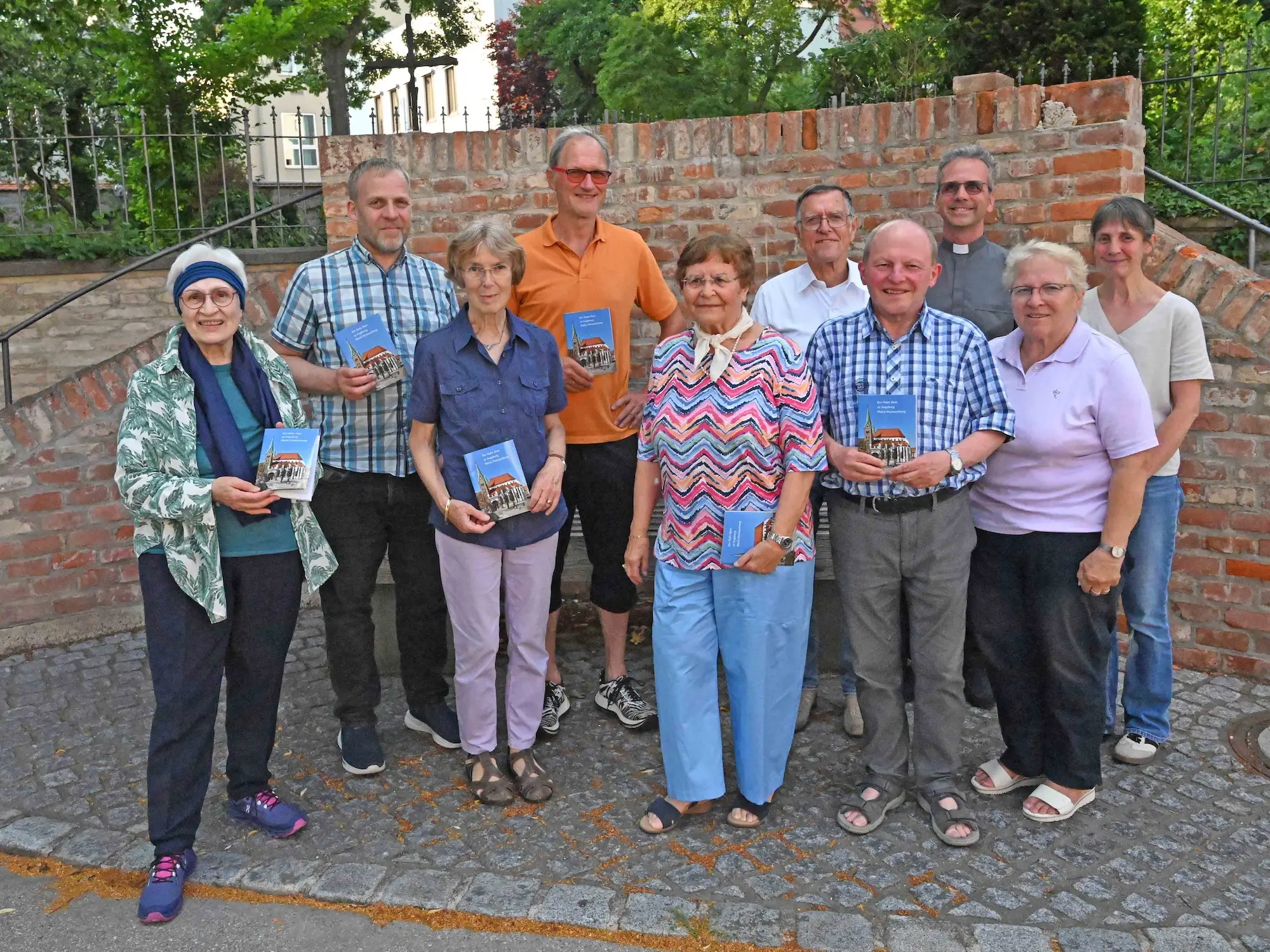 Domführer Augsburger Dom Das Foto zeigt die Domführerinnen und Domführer zusammen mit Domkustos Domkapitular Armin Zürn (dritter von rechts) und dem Autor Dr. Michael A. Schmid (zweiter von links) bei der Vorstellung am 2. Juli 2026, zum Auftakt der Ulrichswoche. Foto: Pressestelle des Bistums Augsburg / Leander Stork
